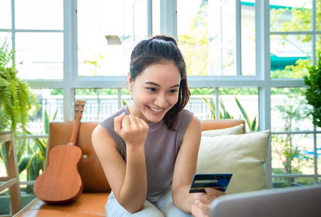 La donna asiatica è in possesso di una carta di credito e utilizza lo smartphone per fare acquisti online a casa. shopping online e-commerce internet banking spendere soldi lavorando da casa concept