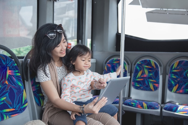 Asian woman is holding her daughter and showing tablet