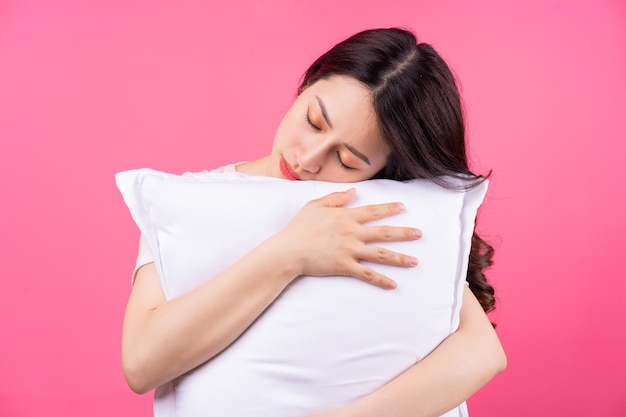 Asian woman is hugging pillow on pink