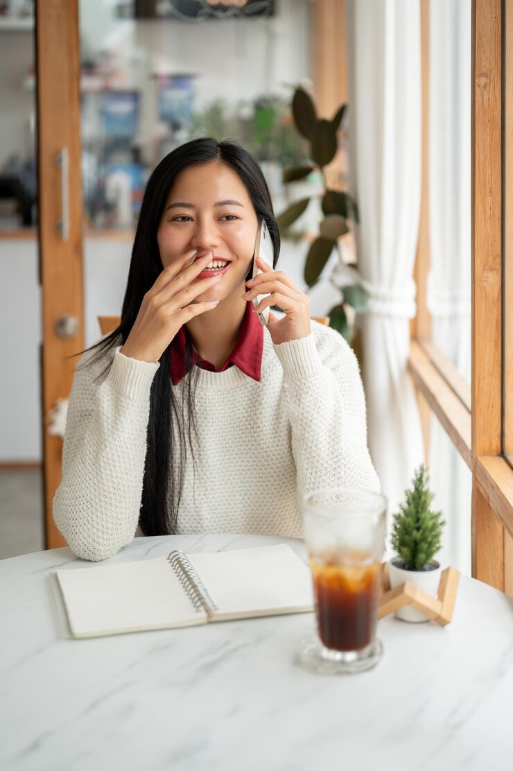 Photo アジアの女性がカフェの大理石のテーブルに座って電話で話している間に笑っています
