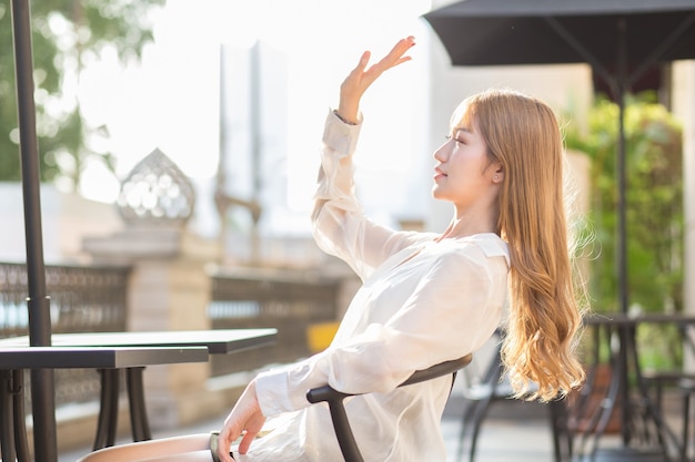 Una donna asiatica è seduta su una sedia e guarda fuori davanti a una caffetteria in una mattina di sole