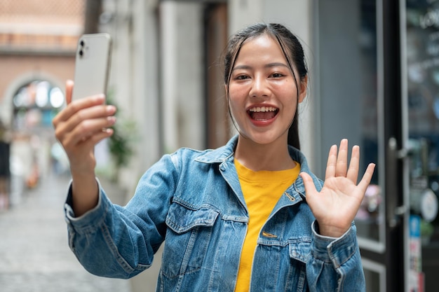 An Asian woman is smiling at the camera talking on a video call while strolling through the city