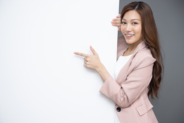 Asian woman is standing behind the white blank banner and pointing to emtry space