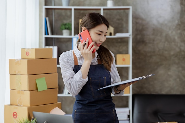 Asian woman is talking on the phone with a customer to confirm an order she owns an online store she packs and ships through a private transport company Online selling and online shopping concepts