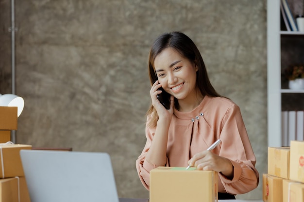 Asian woman is talking on the phone with a customer to confirm an order she owns an online store she packs and ships through a private transport company Online selling and online shopping concepts