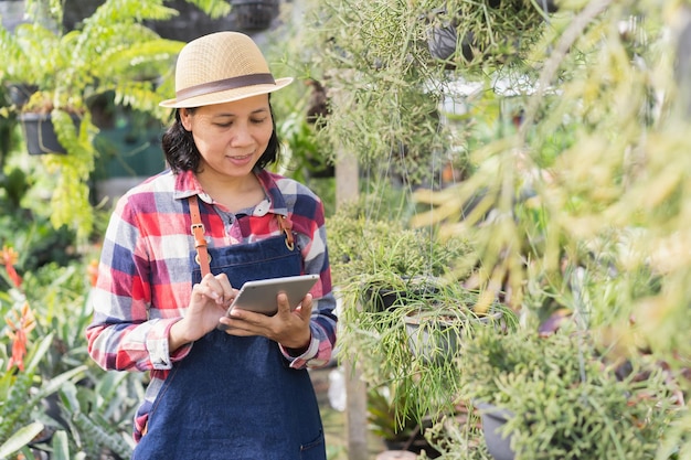 사진 아시아 여성이 태블릿을 사용하여 관상용 식물 가게 스몰 비즈니스 개념에서 식물을 확인하고 있습니다