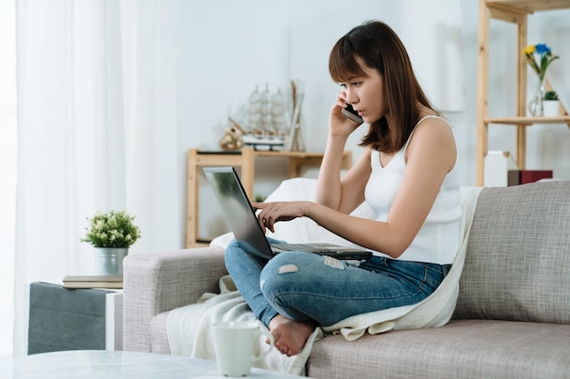 アジアの女性は携帯電話でビジネス会話をしているラップトップを使用しています。日本の実業家は電話でパートナーとアイデアを交換しています。お嬢様がお客様に説明する画面を指さしています。