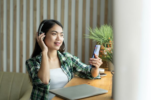 Asian woman in jeans and plaid shirt. Portrait of a young happy female sitting on the couch and working or studying online