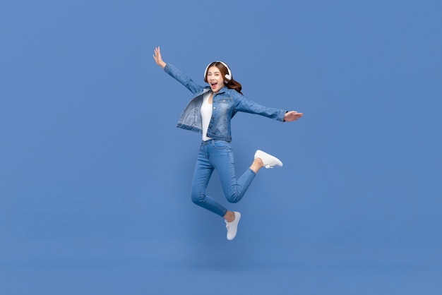 Asian woman jumping while listening to music on headphones