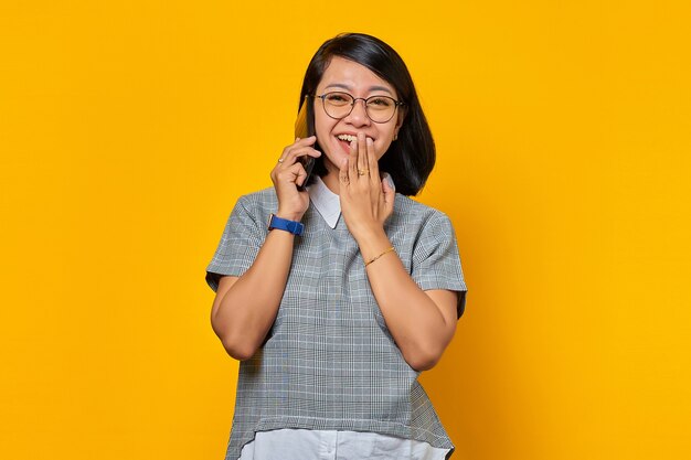 Asian woman laughing while receiving incoming call on mobile phone and covering mouth with hands