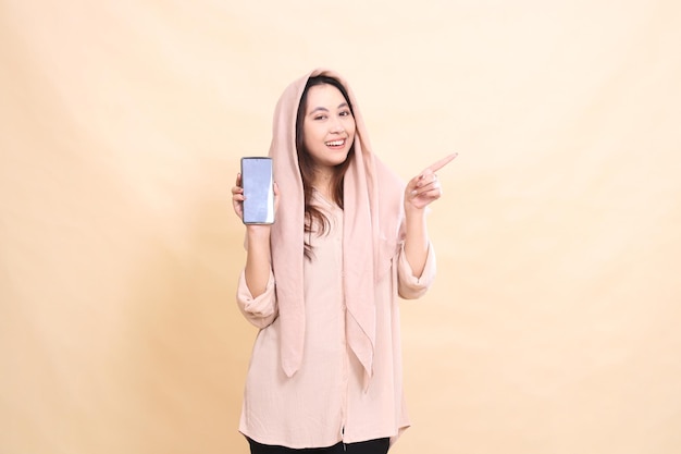 Asian woman laughs cheerfully at the camera with her left hand pointing and holding the cellphone ga