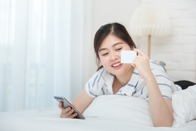 asian woman laying down on bed holding smart phone