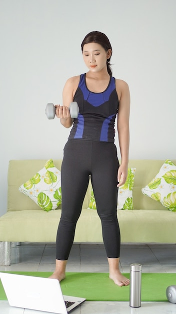 Asian woman lifting half-arm barbell while standing at home