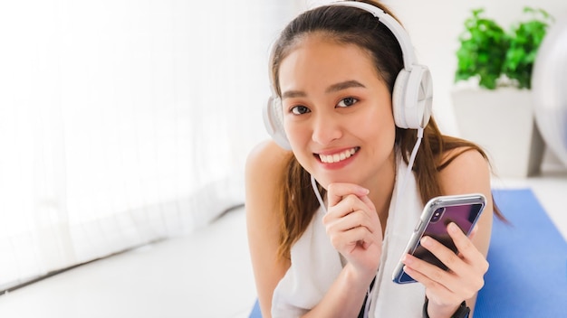 Foto donna asiatica che ascolta musica con cuffie e smartphone dopo aver giocato a yoga ed esercitarsi a casa in background con spazio di copia esercizio per perdere peso aumentare la flessibilità e stringere la forma