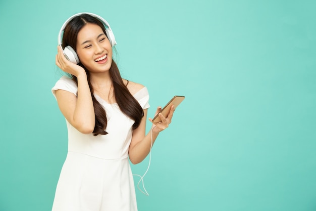 Asian woman listening music with headphones on mobile phone isolated on green background