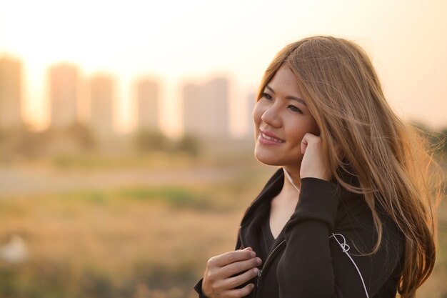 Asian woman listening to music with sunset sky background