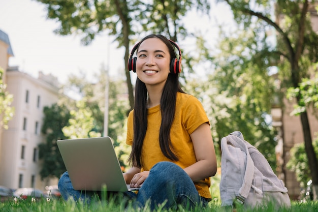 音楽を聴く、草の上に座っているアジアの女性。学生の勉強、通信教育