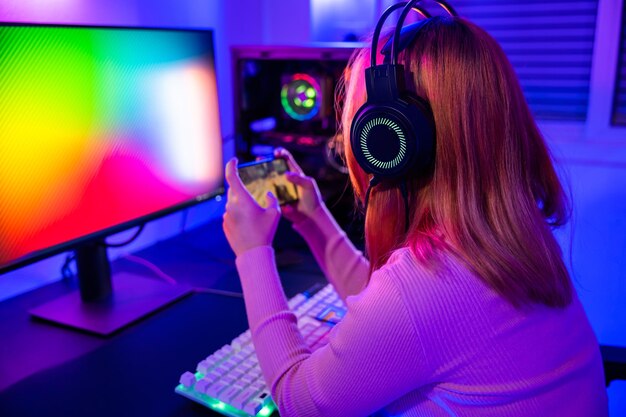 Foto donna asiatica in diretta streaming gioca a videogiochi tramite smartphone a casa luci al neon soggiorno