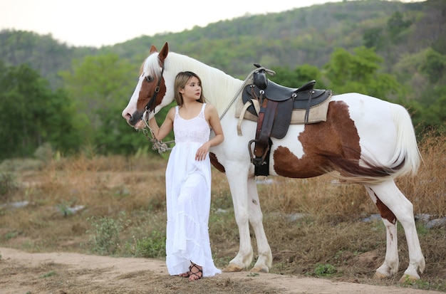 Asian woman in a long dress costume stands with a horse at a cattle farm.