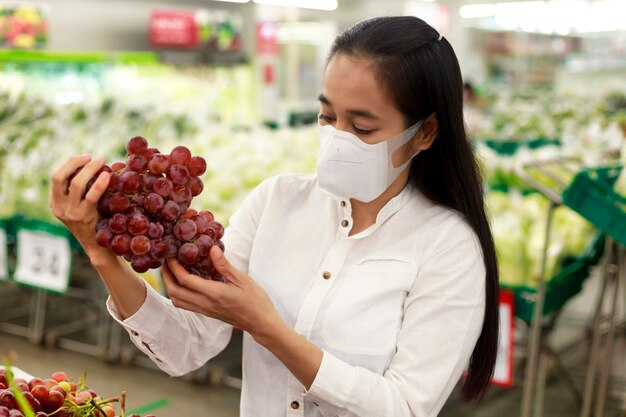Capelli lunghi della donna asiatica che indossa la maschera protettiva nel grande magazzino del supermercato