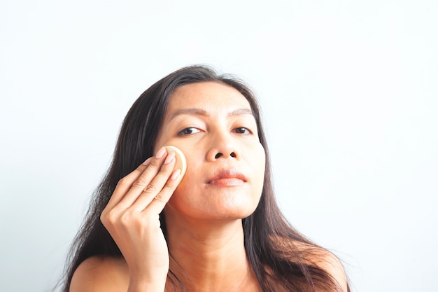 Asian woman looking at camera and applying foundation powder on her face. Beauty concept