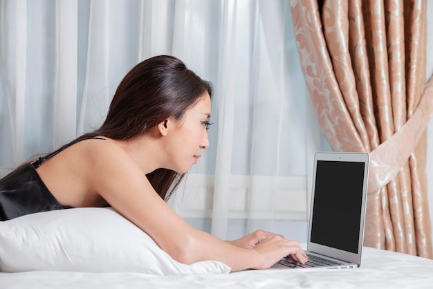 Asian woman lying down while using laptop on the bed