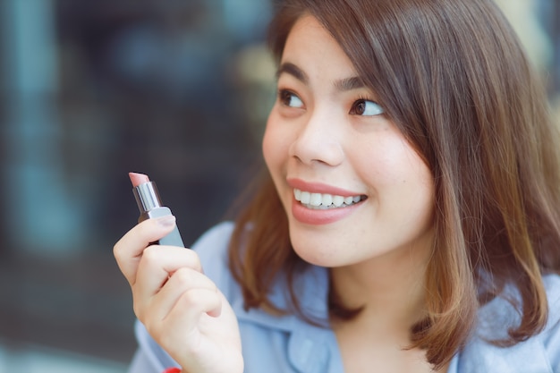 Asian woman make up her face with lipstick in cafe