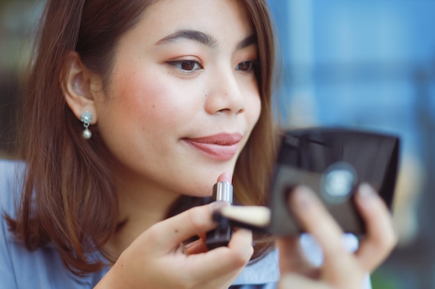 Asian woman make up her face with lipstick in cafe