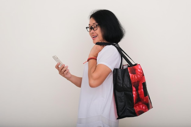 Photo asian woman making a phone call with smartphone in her hand while other hand holding big red shopping bag