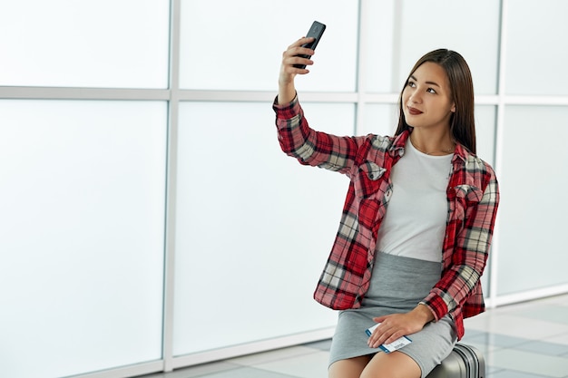 Donna asiatica che fa selfie con i biglietti che aspettano partenza in aeroporto