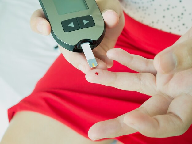 Asian woman measuring glucose level with digital glucose meter, diabetes test