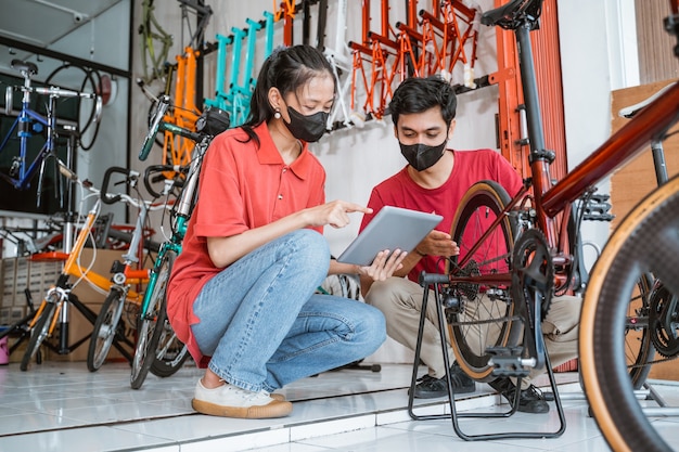 アジアの女性とマスクの整備士がタブレットデジタルで新しい自転車の部品をチェックします