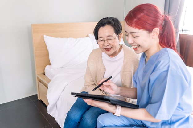 Asian woman nurse wearing scrubs report the health status of Senior Asian woman with digital tablet.