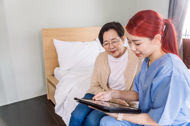 Photo asian woman nurse wearing scrubs report the health status of senior asian woman with digital tablet