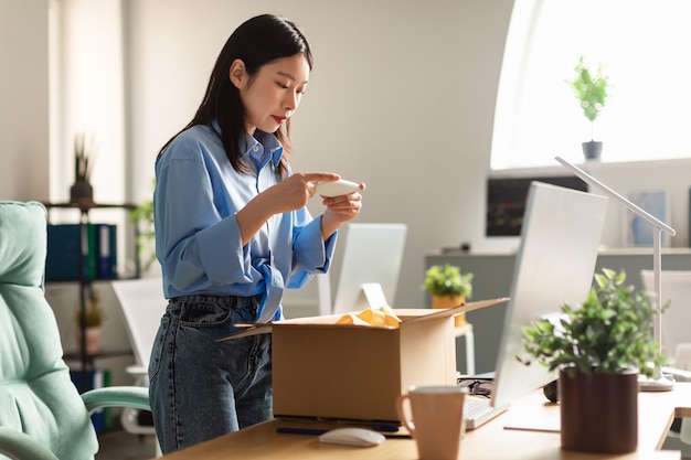 Asian woman packing parcel and taking photo of box