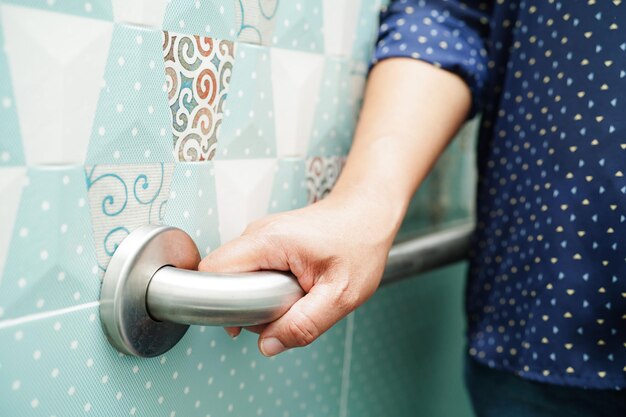 아시아 여성 환자는 간호 병원의 화장실 손잡이 안전 손잡이 바 보안에서 변기 지지 레일을 사용합니다.