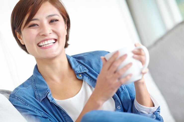 Photo アジアの女性はリラックスするための家の中に平和とコーヒーを飲みソファで週末の休みとして快適です女性は自宅のソファでリビングで顔とラテを飲んで健康の為に自己ケアをしますまたは休日の休みをとります