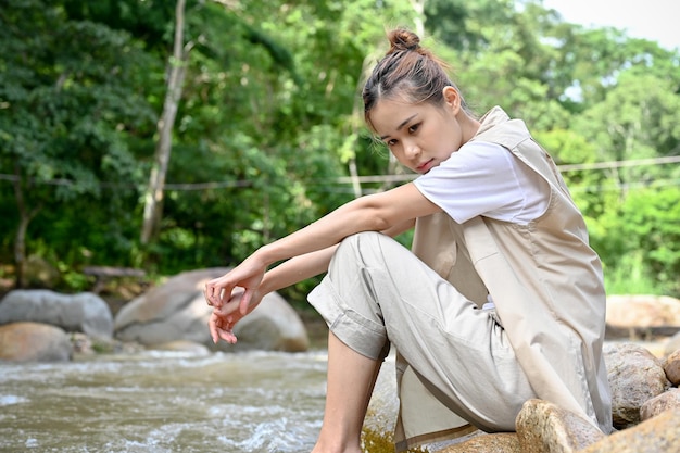 Donna asiatica pensierosa pensando a qualcosa mentre ci si rilassa vicino al bellissimo fiume