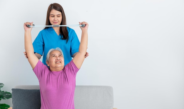 노인 여성의 팔 근육을 지원하기 위해 장비를 사용하는 아시아 여성 물리 치료사
