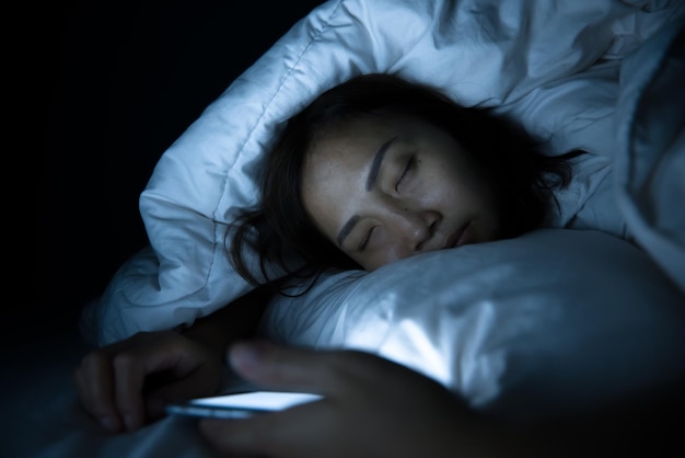 アジアの女性は夜にベッドでスマートフォンを再生しますタイの人々