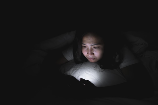 Asian woman play smartphone in the bed at nightThailand peopleaddict news about COVID19 Until cannot sleep