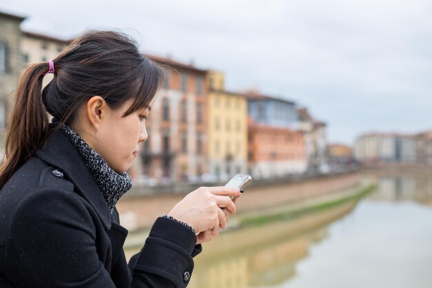 Asian woman play smartphone in river view Pisa Italy.