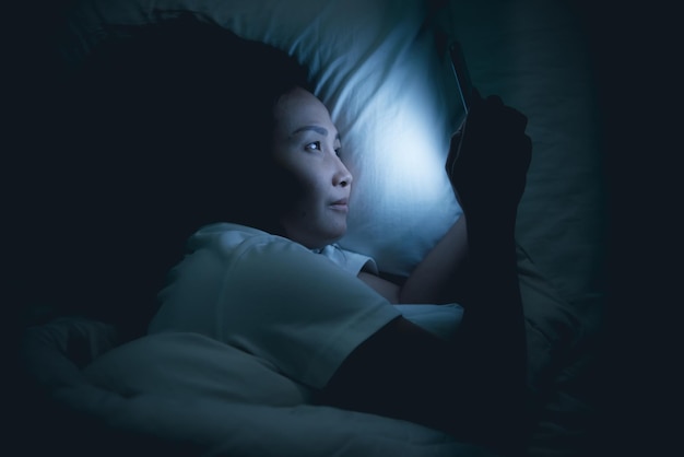 Asian woman playing game on smartphone in the bed at nightThailand peopleAddict social media