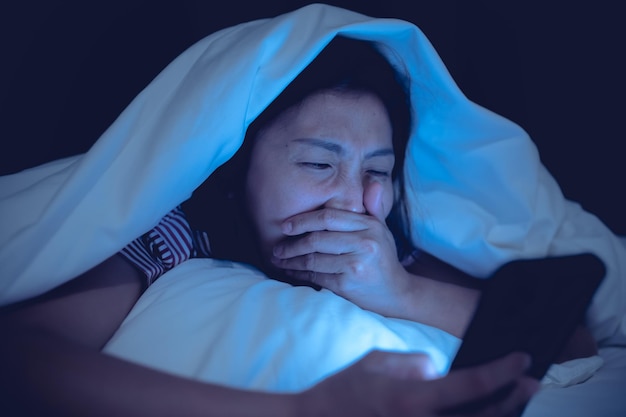 Азиатская женщина играет в игру на смартфоне в постели ночью
