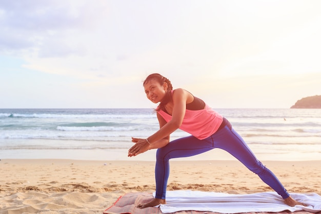 Donna asiatica che gioca yoga ed esercizio sulla spiaggia tropicale in tailandia