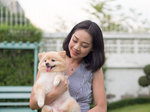 アジアの女性は、彼女のポメラニアンの子犬と庭で遊んでいます。