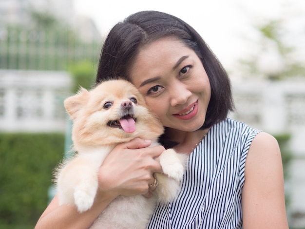 アジアの女性は、彼女のポメラニアンの子犬と庭で遊んでいます。