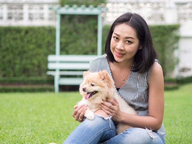 아시아 여자는 정원에서 그녀의 포메라니안 강아지와 함께 재생합니다.