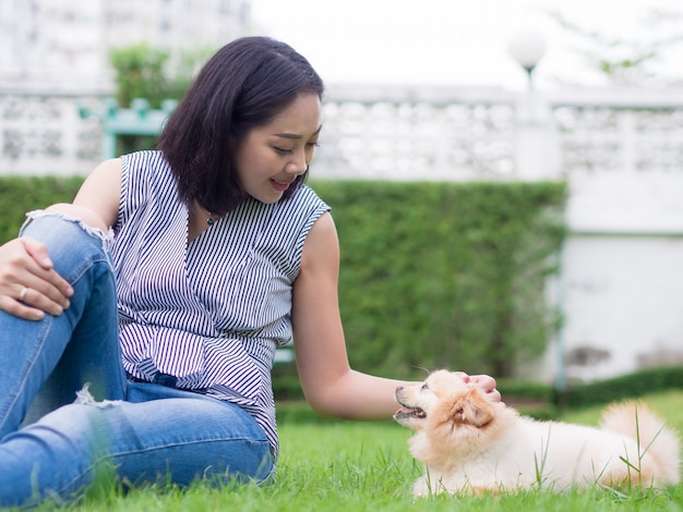 アジアの女性は、彼女のポメラニアンの子犬と庭で遊んでいます。