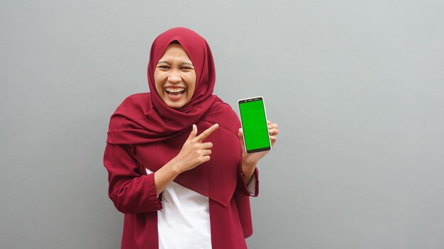 緑色の画面で携帯電話を指しているアジアの女性